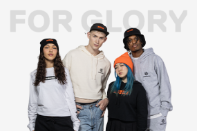 A group of 4 people wearing different versions of SteelSeries gaming apparel, including black hats, orange beanies, a white longsleeve and sweatshirts. Words "For Glory" are behind them.