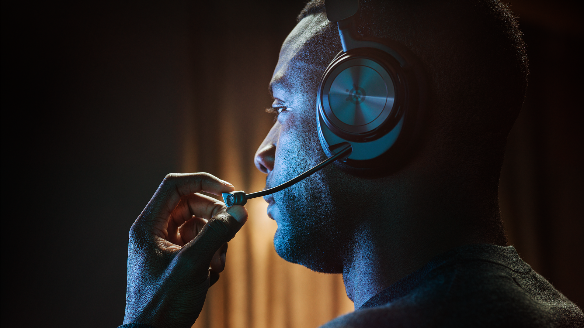 A person sitting with their profile showing off an Arctis Nova gaming headset. They are adjusting the retractable mic.